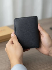 Person holding a black leather wallet on a wooden surface with a blurred background