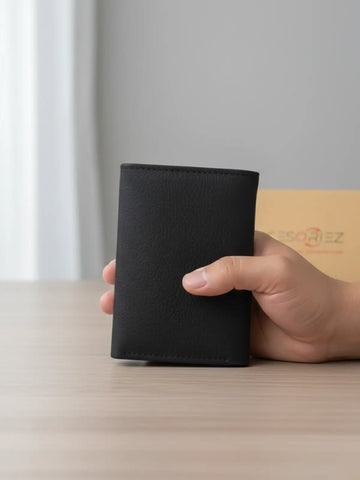 Hand holding a black wallet on a light surface with a neutral background