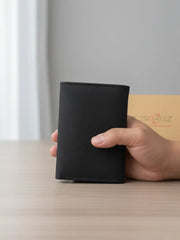 Hand holding a black wallet on a light surface with a neutral background