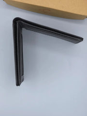 Black metal bracket on a white surface with a cardboard box in the background