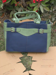 Blue and green handbag on a cardboard surface with plants in the background