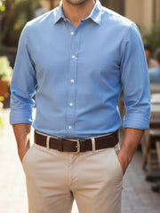 Man wearing a light blue dress shirt and beige pants with a brown belt.