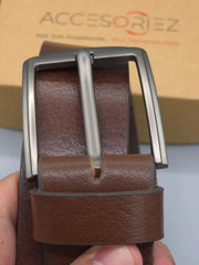Brown leather belt with silver buckle held by a hand, Accesoriez box in the background