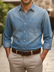 Person wearing a blue denim shirt with rolled-up sleeves and beige pants outdoors.