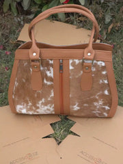 Brown and white cowhide handbag on a cardboard surface with grass in the background