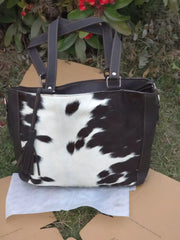Black and white cowhide patterned handbag on a cardboard surface with grass and flowers in the background