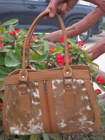 Brown and white cowhide patterned handbag held by a person with flowers in the background