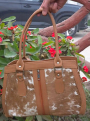 Brown and white cowhide patterned handbag held by a person with flowers in the background