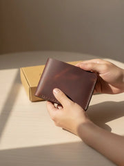 Person holding a brown leather wallet on a light surface with a neutral background