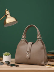 Beige handbag on a wooden surface with a green wall and lamp in the background