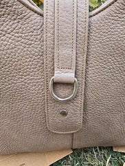 Close-up of a beige leather bag with a silver buckle on a grassy background