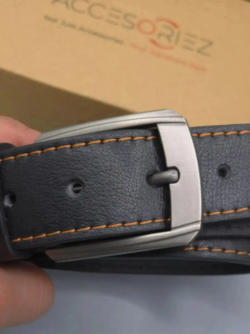 Close-up of a black leather belt with a silver buckle held by a hand, with 'Accesoriz' branding in the background.