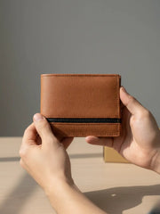 Brown leather wallet held by a person against a neutral background