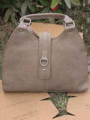 Beige handbag on a cardboard surface with greenery in the background