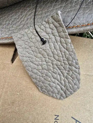 Close-up of a textured gray leather patch with stitching details on a cardboard surface.