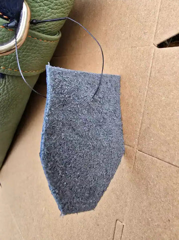 Gray felt patch on cardboard with green leather item in background