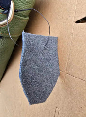 Gray felt patch on cardboard with green leather item in background