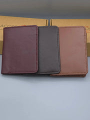 Three leather wallets in different colors on a light gray surface with a cardboard box in the background.