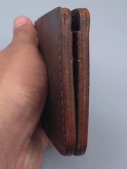 Brown leather wallet held by a hand against a gray background