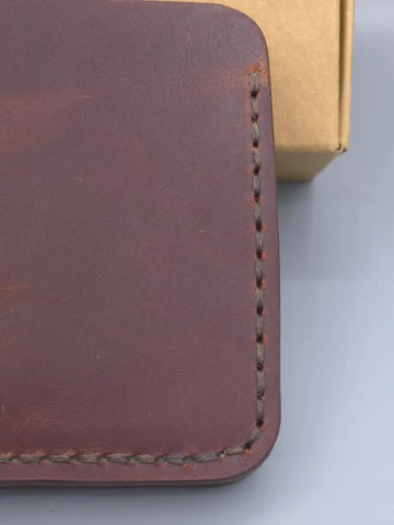 Close-up of a brown leather wallet with visible stitching on a light gray background
