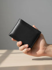 Hand holding a black leather wallet against a neutral background
