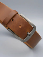 Brown leather belt with a silver buckle on a light gray background