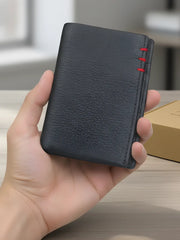 Black leather wallet with red stitching held in a hand against a neutral background