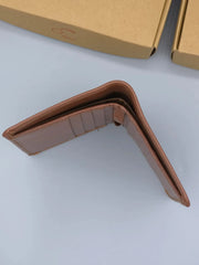 Brown leather wallet on a light gray surface with a cardboard box in the background.