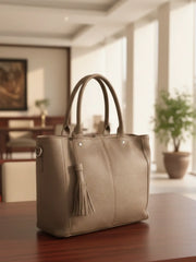 Beige handbag with a tassel on a wooden surface in a blurred indoor setting