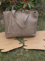 Beige handbag with a tassel on a cardboard stand against a natural background