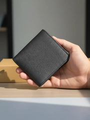 Hand holding a black leather wallet on a wooden surface with a blurred background